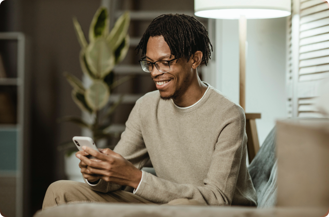 Black man wearing beige looking to his smartphone and smiling